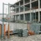 Stalen bouwhek op Europese bouwplaats met grondankers, klemmen en A-frames op kasseien, betonnen gebouw op achtergrond.