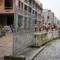 Gegalvaniseerd stalen bouwhek op een Europese bouwplaats met betonnen barriers en arbeiders in veiligheidsvesten op de achtergrond.