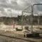Gegalvaniseerd stalen bouwfence met gewichtsbasis op Europese stedelijke bouwplaats, puin op winderige bestrating, stadssilhouet op achtergrond.