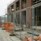 Gegalvaniseerde stalen hekken op betonnen stoep voor half-afgebouwde bakstenen gevel, bouwplaats in Noord-Europa.