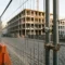 Tijdelijk bouwhek met gegalvaniseerde klemmen en verzwaarde voeten op Europese straatweg met kasseien en betonnen gebouw op achtergrond.