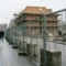Tijdelijke bouwafzetting van gegalvaniseerd staal met betonnen voeten op een Nederlandse stoep, onafgewerkt bakstenen gebouw op achtergrond.