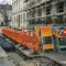 Oranje verkeersbarricades en stalen borden op Europese stedelijke bouwplaats met opgebroken asfalt en zichtbare steigers op de achtergrond.