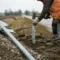 Wegwerker in oranje veiligheidsvest slaat grondanker voor verkeersbordpaal in Europese wegberm.