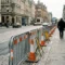Galvaniseerde stalen bouwbarrières met oranje verkeerskegels op Europese kasseienstraat, klassieke architectuur op achtergrond.
