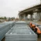 Gestapelde gegalvaniseerde staalomheiningen op Europese infrastructuurlocatie met betonnen viaduct in aanbouw op achtergrond.