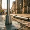 Gegalvaniseerde stalen grondanker in vers beton gegoten op Europese straatlocatie met geplaatste verkeersmast en kobbelstenen achtergrond.