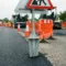Gegalvaniseerde stalen grondpotanker voor tijdelijk verkeersbord op Europese wegwerkplek met oranje barriers en vers asfalt.