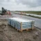 Pallet met verzinkte stalen grondpotten op een Nederlandse infrastructuurlocatie, met een polderlandschap op de achtergrond.