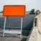 Oranje tijdelijk verkeersbord op stalen A-frame standaard langs Europese snelwegwerkzaamheden met vers asfalt en veiligheidspaaltjes.