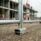 Gegalvaniseerd stalen bouwhek met gelaste maasverbindingen en klemvoeten op grindondergrond, betonnen bouwstructuur op de achtergrond.